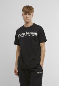 Melnas kokvilnas t-krekls ar baltu tekstu "bruno banani" un "NOT FOR EVERYBODY" uz priekšpuses. Īsas piedurknes, apaļa izgriezuma kakla izgriezums, brīva piegriezuma. 