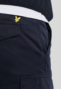 Marineblauwe katoenen cargoshorts met stikdetails en zijzakken. Bevat een gele geborduurde logo op de tailleband.