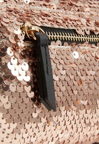 Primo piano di un tessuto in paillettes dorate con una cerniera dorata e un tirante in pelle nera su una borsa o un capo d'abbigliamento.