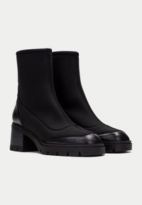 Botines negros con un upper de tela suave, puntera de cuero y suela de tacón grueso que presenta un patrón texturizado y tracción con tacos.