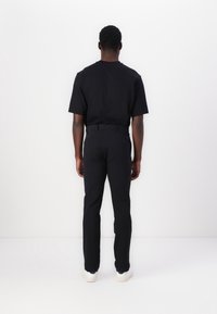 Sort T-shirt med korte ærmer, parret med sorte bukser. Begge beklædningsgenstande har en glat tekstur og en tætsiddende design. Hvide sneakers med en struktureret sål.