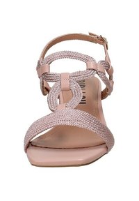 Sandalo rosa chiaro con cinturini intrecciati, suola piatta, fibbia alla caviglia e design ad anello intricati. Materiale liscio con una texture morbida.