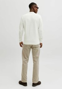 Pull blanc texturé à manches longues avec un col rond, associé à un pantalon en velours côtelé beige clair et des chaussures marron foncé.