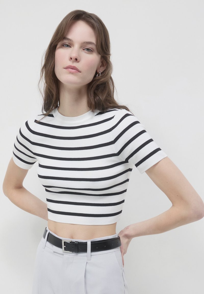 T-shirt cropped a righe bianche e nere con texture a costine e maniche corte, abbinato a pantaloni grigi chiari a vita alta e una cintura nera.