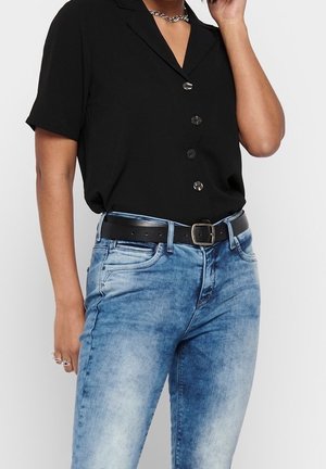 Czarna, krótka koszula z kołnierzykiem i guzikami, zestawiona z jasnoniebieskimi jeansami i czarnym paskiem z metalową klamrą.