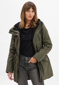 Parka imbottito verde oliva con colletto foderato in fleece nero, chiusure a cerniera e a bottone, vita regolabile con coulisse e numerose tasche.