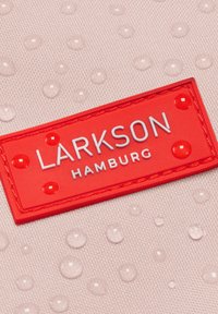 Czerwony prostokątny etykieta z napisem "LARKSON HAMBURG" na różowej teksturowanej tkaninie z kroplami wody.