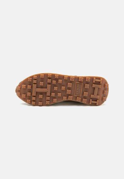 Suela de zapato de goma marrón con tracción cuadrada y un logo central. Diseño robusto destinado a la tracción y durabilidad.