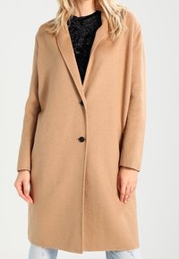 Beige uldblandingsfrakke med reverskrave, frontlukning med knapper og lange ærmer. Glat tekstur med skræddersyet, lige snit.