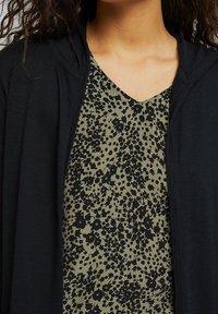 Black hooded cardigan layered over an olive green top with a black floral print. Fabric appears soft with a smooth texture and v-neck design.