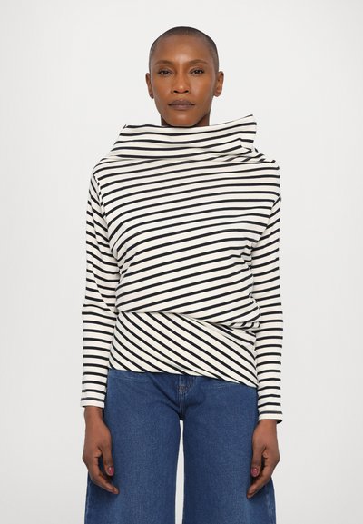 Haut à manches longues avec col drapé en crème et rayures horizontales noires, associé à un jean bleu taille haute. Tissu doux et extensible.