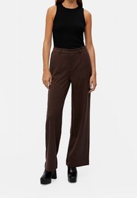 Pantalon large marron en tissu lisse avec des plis à l'avant. Associé à un haut noir sans manches et des chaussures plateformes noires épaisses.