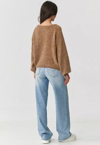 Brązowy sweter z dzianiny o luźnym kroju i ściągaczu, połączony z jasnoniebieskimi spodniami typu wide-leg i białymi tenisówkami.