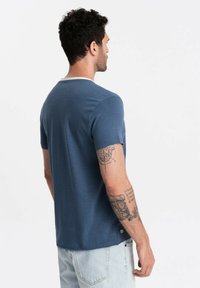 Niebieska koszulka polo z krótkim rękawem, okrągłym dekoltem i kontrastowym białym wykończeniem w okolicy szyi. Posiada luźny krój i miękką fakturę.