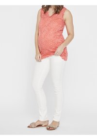 Korálový krajkový bezrámový top s vlnitým lemem, spárovaný s bílými přiléhavými kalhotami a béžovými sandály s třásněmi.