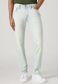 Lys vaskede denimjeans med lige ben. Har fem lommer, kontraststing og lynlås. Sammen med hvide sneakers.