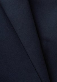 Gros plan sur un tissu bleu marine foncé avec une texture fine visible de tissage diagonal et des plis superposés.