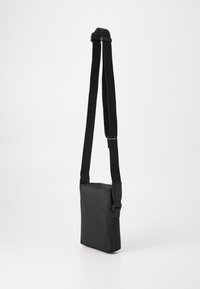 Sac bandoulière noir avec une surface texturée. Doté d'une sangle ajustable et d'une fermeture éclair supérieure sécurisée. Forme rectangulaire compacte.