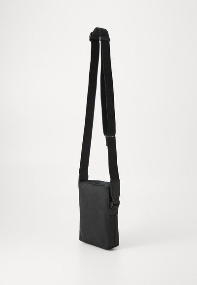 Sac bandoulière noir avec une surface texturée. Doté d'une sangle ajustable et d'une fermeture éclair supérieure sécurisée. Forme rectangulaire compacte.