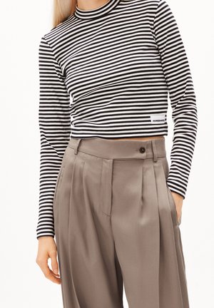 Kobieta ubrana w czarno-białą, paskowaną, długorękawową, skróconą bluzkę oraz wysokiej talii taupeowe plisowane spodnie z zapinanym na guziki pasem.