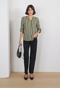 Olive green striped blouse with a buttoned collar, paired with black tailored pants. The model holds a small black handbag.