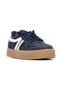 Zapatillas de color azul marino con acentos curvados en blanco, cuello acolchado y diseño con cordones. Presentan una suela de goma gruesa de color marrón claro.
