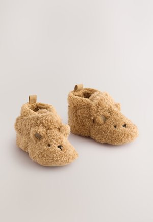 Chaussons beiges et duveteux avec un motif de visage d'ours, dotés d'une texture douce, d'un bout arrondi et d'une boucle à l'arrière pour un enfilage facile.