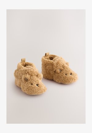 Karamelni, puhasti copati z motivom medvedjega obraza, z mehko teksturo, zaobljenim prstnim delom in zanke na hrbtni strani za enostavno obuvanje.