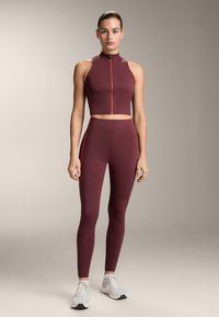 Bordó sportmelltartó magas nyakkal és cipzárral, hozzáillő feszes leggings, melyeket kontrasztos narancssárga oldalsávok díszítenek, rugalmas anyagból készült.