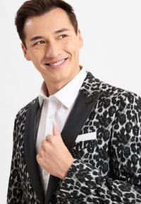 Leopardenmuster-Blazer in Schwarz und Weiß mit einem satinblauen schwarzen Revers und einem weißen Hemd darunter. Bemerkenswerte Details sind ein weißes Taschentuch.