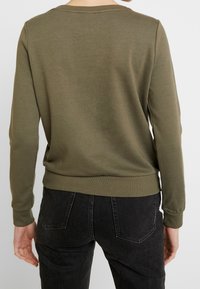 Sudadera verde oliva de manga larga, con escote redondo acanalado y dobladillo; fabricada en una suave mezcla de algodón con un corte relajado y un diseño minimalista.