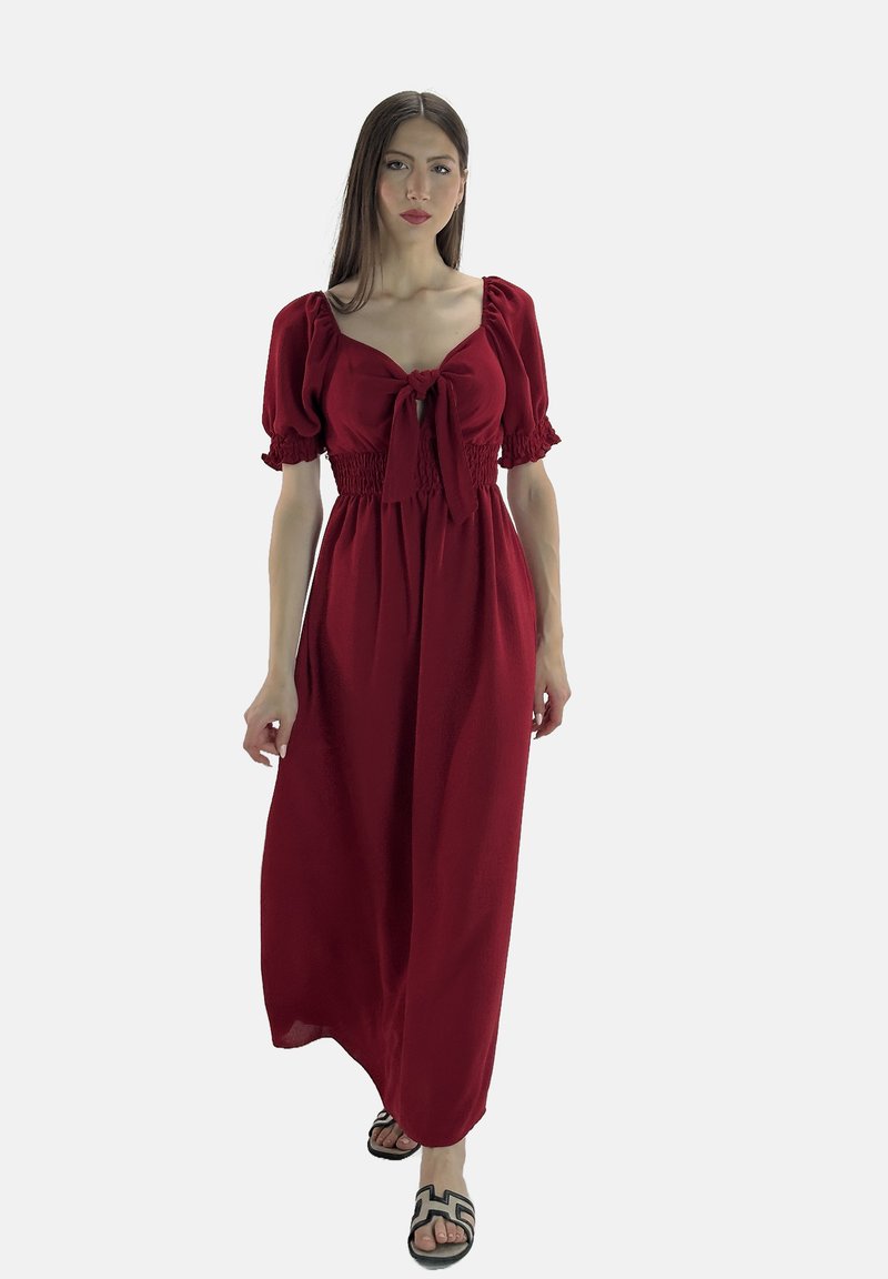Rotes Maxikleid mit kurzen Puffärmeln, gebundenem Vorderteil, gerafftem Taillenbereich und fließendem Rock. Kombiniert mit schwarzen, gemusterten Sandalen.