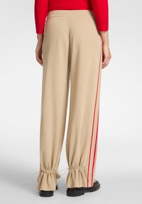 Beige wijde broek met rode zijstrepen, gecinchde enkels en een zachte textuur. De tailleband is elastisch, wat het comfort en de pasvorm verbetert.