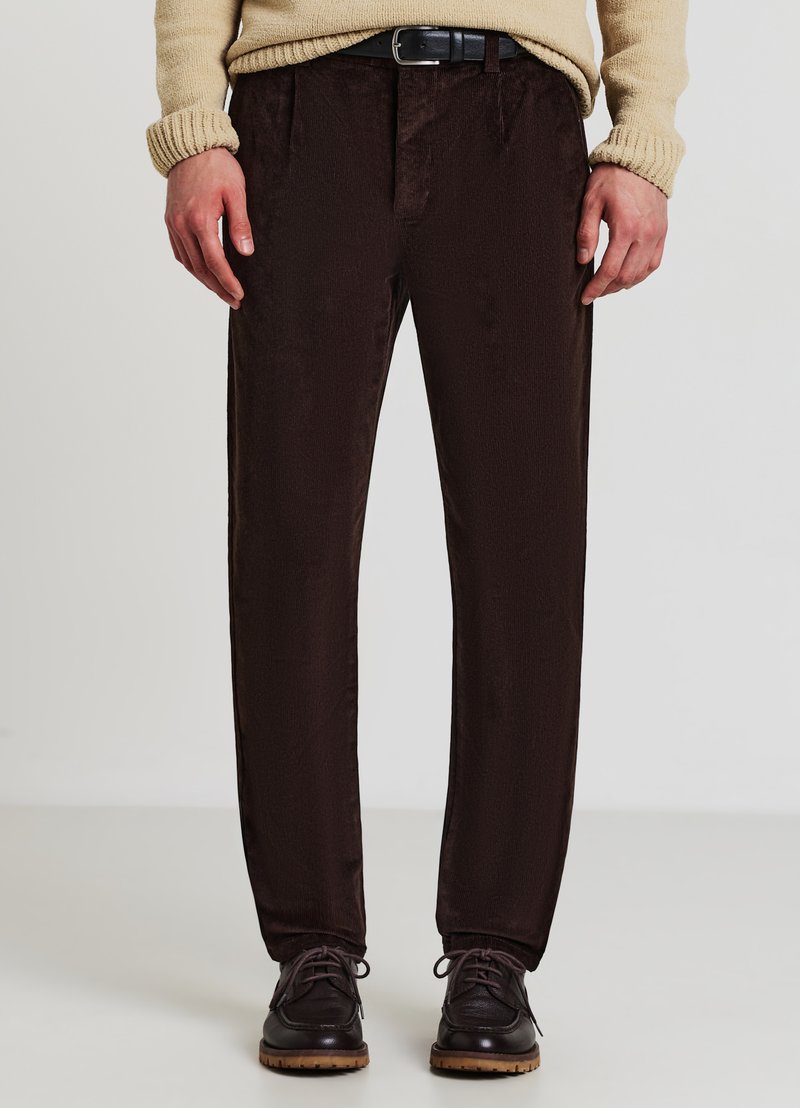Pantalons en velours côtelé marron avec une coupe droite, présentant une texture subtile et une taille. Associés à des chaussures noires à lacets.