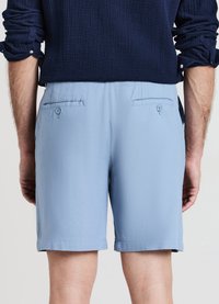 Hellblaue Shorts mit strukturierter Oberfläche, zwei Gesäßtaschen mit Knopfverschluss. Fransensaum, lockere Passform und mittlere Oberschenkel-Länge.