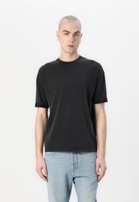 Svart bomullströja med uppvikta korta ärmar, rund hals och avslappnad passform. Buren med ljusblå denimjeans.