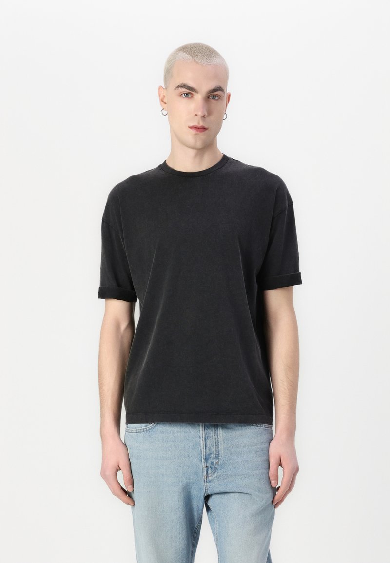 Zwarte katoenen t-shirt met opgerolde korte mouwen, ronde hals en een relaxte pasvorm. Gekenmerkt met lichtblauwe denim jeans.