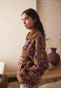 Brązowy sweter z haftowanymi wzorami kwiatowymi w kolorze fioletowym i kremowym, z zamkiem błyskawicznym przy kołnierzu oraz miękkim, teksturowanym materiałem.