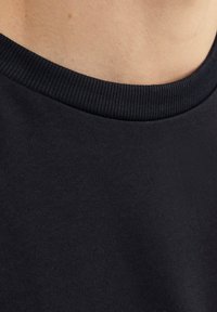 Camiseta de algodón negra con cuello acanalado y una textura suave. El tejido parece ligero y flexible.