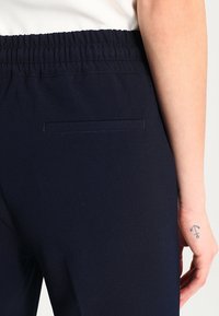 Granatowe spodnie z elastycznym paskiem w talii o gładkiej fakturze, z pojedynczą kieszenią z tyłu i minimalnymi detalami szwów.