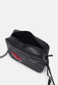 Czarna pikowana torba o gładkim wykończeniu, z czerwonym sercem i białym napisem. Posiada łańcuszkowy pasek i zamek błyskawiczny.