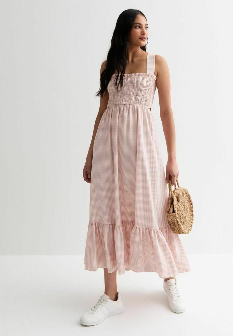 Roze geruite maxi-jurk met een geschuurd lijfje, brede banden en een gerimpelde zoom. Gepaard met witte sneakers en een kleine gevlochten handtas.