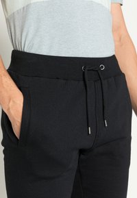 Schwarze Trainingshose mit elastischem Bund und Zugbanddetails. Verfügt über seitliche Taschen und eine weiche Textur. Lässige Passform.