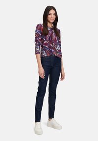 Maglietta a maniche lunghe con una stampa paisley multicolore, abbinata a jeans aderenti blu scuro e sneakers bianche con la piattaforma.