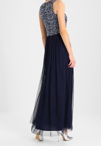 Lång marinblå klänning med en texturerad, utsmyckad bodice och en flödande genomskinlig kjol. Bärs med silverfärgade högklackade skor.