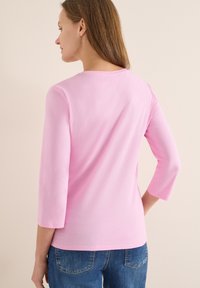 Chemise rose clair à manches longues en tissu doux, avec un col rond et une coupe décontractée, associée à un jean denim bleu.