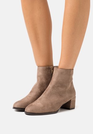 Beige ruskinds ankelstøvler med firkantet tå og lav blokhæl, med en sidelukning for nem påklædning. Glat tekstur og tætsiddende design.