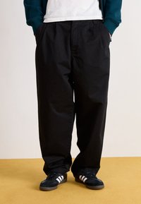 Svarta bomullsbyxor med en avslappnad passform, med sidfickor och en slät yta, kombinerade med svarta träningsskor med vita ränder.