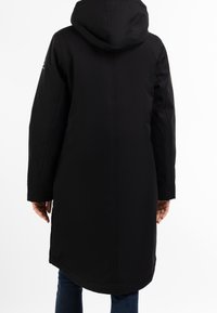 Sort, lang regnfrakke med hætte. Har en lige skæring og glat tekstur. Indeholder sidesømme og et diskret logo på ærmet.