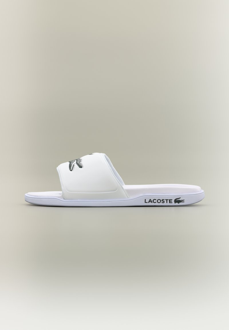 Bijela Lacoste lađa sandala s širokim remenom, teksturiranim logotipom i gumenim potplatom. Glatka površina i minimalistički dizajn.